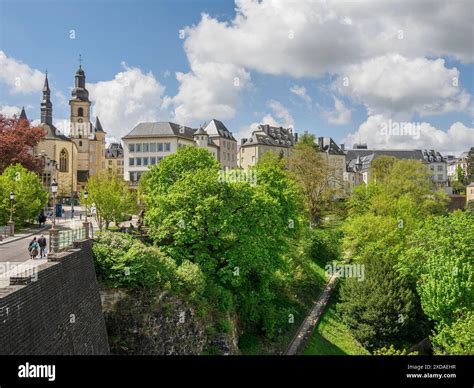 Cityscape of Luxembourg with historic buildings and towers, surrounded by greenery and sunny ...