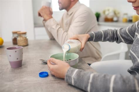 Girl pouring milk from a bottle into a plate with porridge, sitting at ...