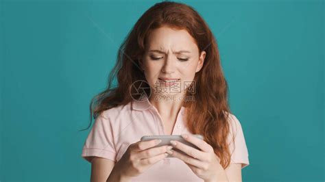有吸引力的神经紧张的红发女孩在多彩背景上玩智能手机游戏高清图片下载-正版图片504362854-摄图网