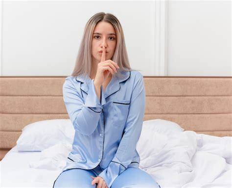 Jovem mulher bonita de pijama azul sentada na cama fazendo gesto de ...