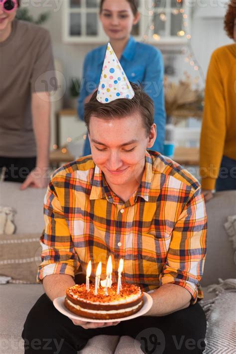 Make a wish. Man wearing party cap blowing out burning candles on ...