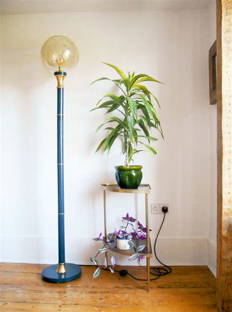 A gold and navy floor lamp with a vintage glass globe shade ...
