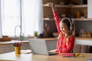 Cute little girl raising hand during online lesson on laptop at home ...
