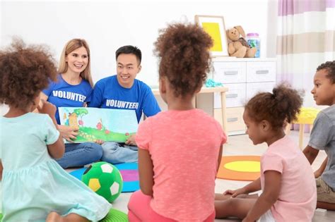 Young volunteers reading book with little children in light room ...