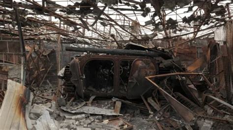 A man walks past a burnt armoured personnel carrier near buildings destroyed in the course of Ukrain