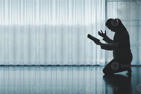 silhouette of woman kneeling and praying in modern church at sunset ...