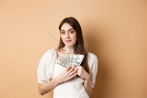 微笑的富有女人展示美元钞票，在镜头前看起来很高兴，赚钱或快速贷款现金，站在米色背景上高清摄影大图-千库网
