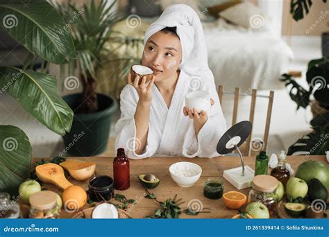 Young Asian Woman in White Bathrobe and Towel Holding Half of Coconut and Making Homemade Cream ...