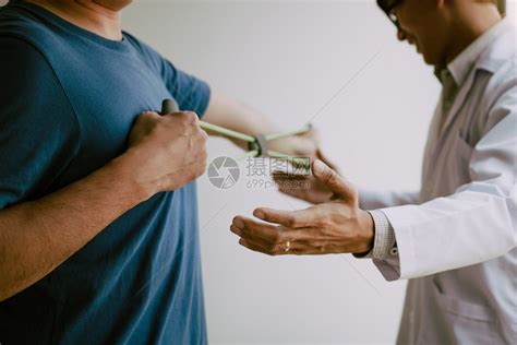 亚洲年轻男理疗师帮助病人在办公室里举起哑铃锻炼高清图片下载-正版图片305702277-摄图网