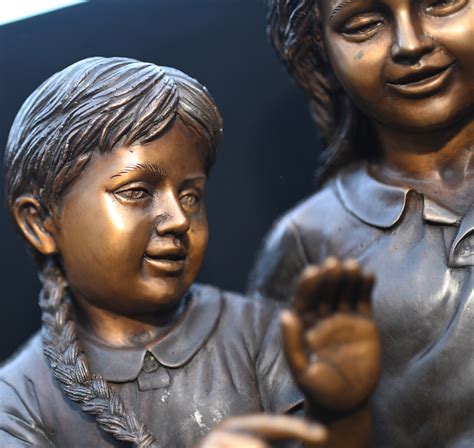 Colored outdoor statue of a child pressing their forehead on the hand of a seated elder