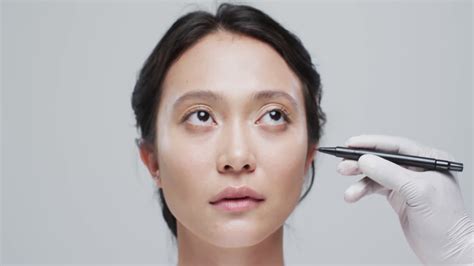 Hand in glove examining face of asian woman on grey background, slow ...