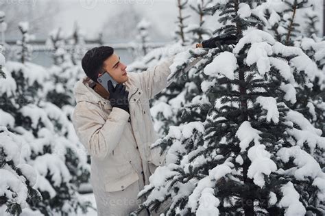 Man walking outdoors, talking by the phone and choosing christmas tree ...