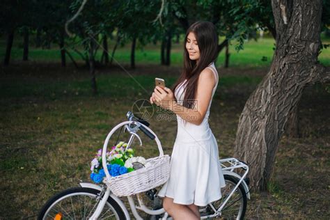 身穿白裙子的女孩和手拿着智能手机的背心站在一辆自行车旁边高清图片下载-正版图片506509636-摄图网