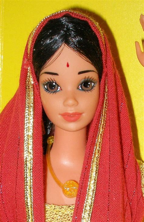 a doll wearing a red and gold sari with an orange head piece on it's head