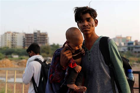 A migrant worker carries his child, as they wait to cross the border to ...