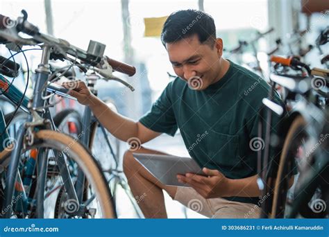 Handsome Young Entrepreneur Squatting To Check a Bicycle Frame Using a Tablet Stock Image ...