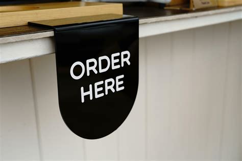 The order here sign in white letters on a black plastic sheet hanging ...
