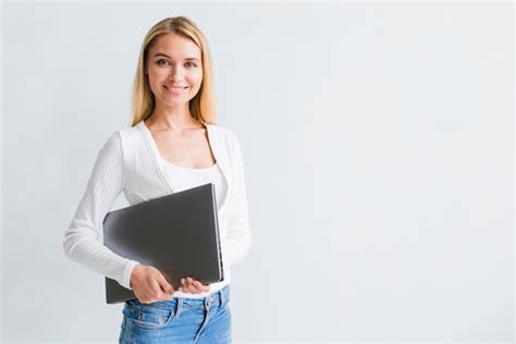 Lächelnde dünne blonde Frau in den Jeans mit schwarzem Laptop ...