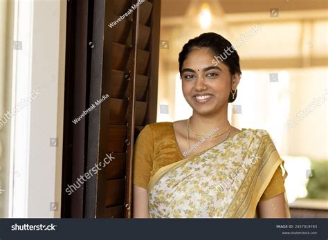 Shamima Begum leaning against a door frame. She has long dyed brown hair and is wearing sunglasses with a light grey top underneath a sweatshirt jacket