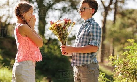 Happy boy and girl standing in a park with the boy giving a bouquet of ...