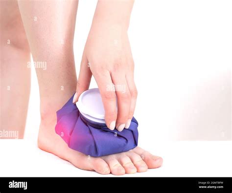 A girl applies a medical blue ice pack to the muscles of the lower leg to relieve pain and ...