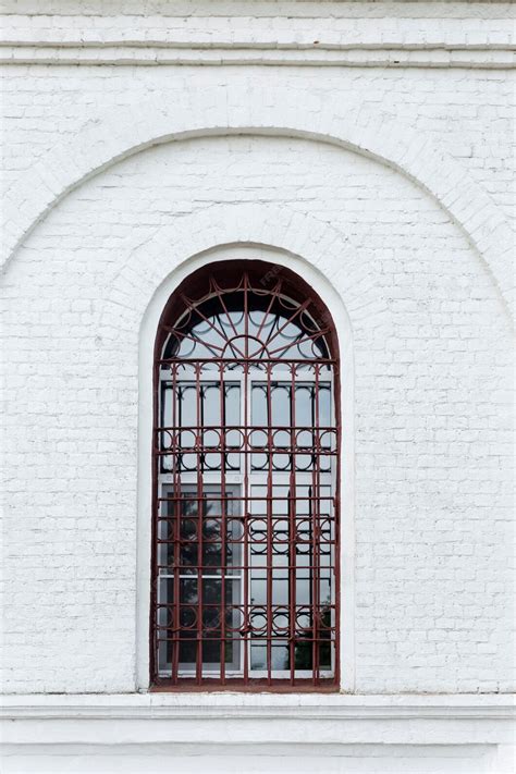 An old arched window behind bars in an old white brick building ...