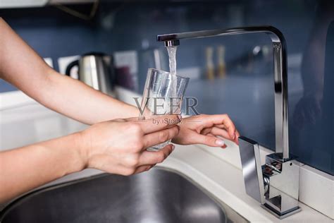 在厨房水槽往玻璃杯里注水的女人照片摄影图片_ID:162614217-Veer图库