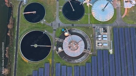 Top-down aerial drone footage of a modern wastewater treatment plant with circular settling tanks and solar panels, showing sustainable water management and renewable energy