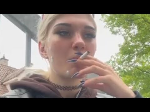 A biker girl smokes a cigarette, opens a new pack, spits, and litters.