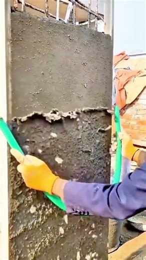 Worker Using a Straightedge to Level Fresh Cement Plaster on a Concrete Wall