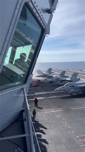 A parked fighter jet suddenly explodes on the flight deck of an aircraft carrier.