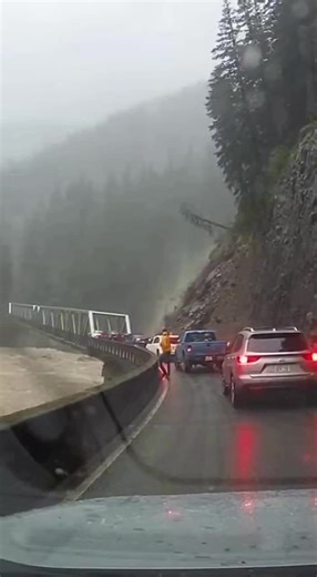 Landslide Collapses Bridge as Traffic Backs Up Along Mountain Highway British Columbia, Canada — A sudden landslide sent tons of mud, rock, and debris crashing down a mountainside, wiping out part of a bridge and forcing traffic to a standstill as drivers watched in disbelief from just yards away. Video captured from inside a vehicle shows a dense brown wave of earth pouring down the slope beside a narrow mountain roadway. The debris surges with startling speed, slamming into the bridge structur
