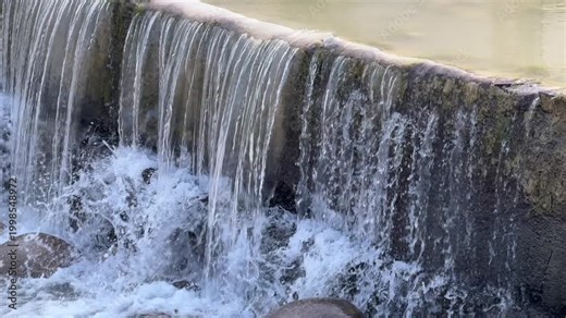Water cascading over concrete spillway, smooth flowing waterfall, urban water system and flow concept, close up texture background