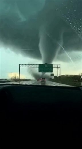 Tornado Touches Down Over Highway as Drivers Race for Safety Near a major interstate, late afternoon — A massive tornado touched down directly over a busy highway, forcing drivers to confront a terrifying wall of rotating wind and debris as traffic continued beneath darkening skies. The funnel cloud formed rapidly, descending from a low, turbulent storm system and stretching toward the pavement just ahead of moving vehicles. Dashcam footage shows cars traveling beneath overhead road signs as the