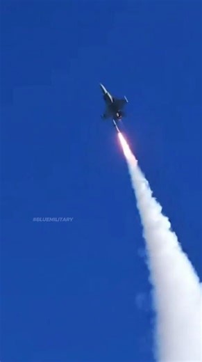A fighter jet executing a vertical climb while launching a missile straight into the blue sky.