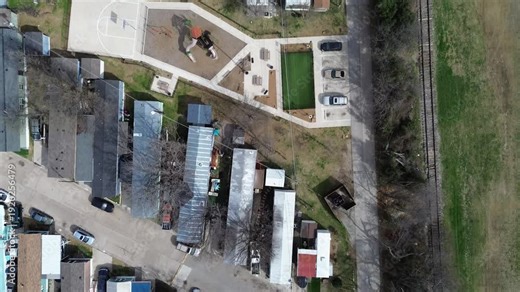 Small park and playground sit east of RV trailer mobile homes community dense grid near rail corridor running parallel to neighborhood edge. Bright court surfaces, winter bare trees, Plano, Texas