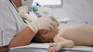 child health, male kid nurse wearing gloves, holds an oxygen mask on his face to inject little patient into anesthesia before heart surgery in a hospital ward