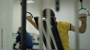 Classes in the sports hall for people with disabilities. A person performs an exercise to strengthen the muscles of the arms and neck.