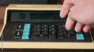 Counting on a vintage calculator. Male hand press buttons on an old retro calculating machine close-up on a wooden desk. Concept counts home finances, currency, savings, financial bills.