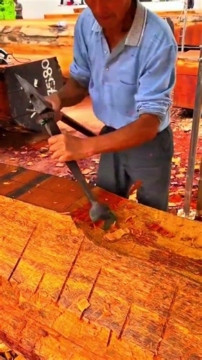 Smoothing the surface of a large wooden log using a long-handled chisel for precise shaping
