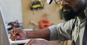 Carpenter writing in notepad while using computer