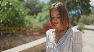 Attractive cheerful lady in elegant white drees walking street garden with flowers, charming smiling to camera. Travel in Turkey, Datcha