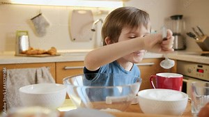 Funny laughing little boy eating creme for baking pie with spoon. Children cooking with parents, little chef, family having time together, domestic kitchen.