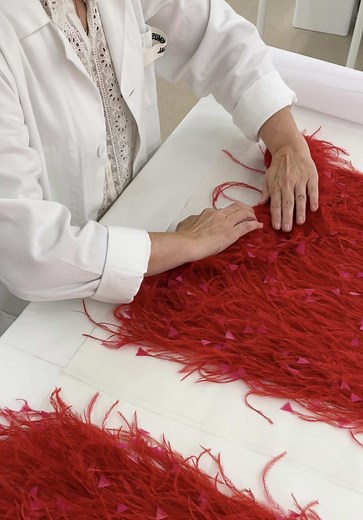 Making the #Jacquemus La Robe Grenadine from the « Le Bonheur » collection. Featuring red dyed ostrich featherwork, the feathers are first assembled into delicate bunches of two to five feathers. Each bunch is then meticulously attached by hand onto a white organza base in a cascading arrangement, creating a soft gradient effect. Pink turkey feathers, cut into small triangular shapes, are then applied to add texture and depth to the composition. The skirt features a total of 2,797 ostrich feathe