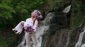 Groom holds bride in his arms near waterfall. Wedding couple. Happy family.