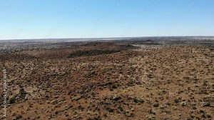 An extreme long shot that captures the landscape of shrubby terrain against a clear blue sky. The camera is lowered gradually revealing hilly features that form part of the landscape as well.