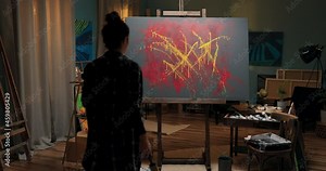 Talented painter spends evening in front of canvas devotes time to abstract work, in hand holds can of yellow paint and brush, girl splashes color on painting, artistic vision