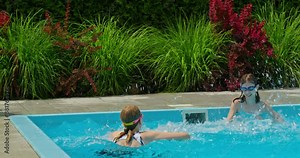 Two teenage girls joyfully splashing water in a pool. Slow-motion video captures their playful fun.