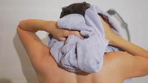 Woman wipes her wet hair with terry towel. Daily routine in white bathroom.
