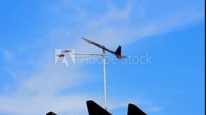 Wind vane turning towards wind, clear blue sky partially cloudy in the background. Weather instrument.